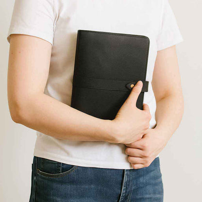 Person holding a black leather refillable notebook cover against a plain background